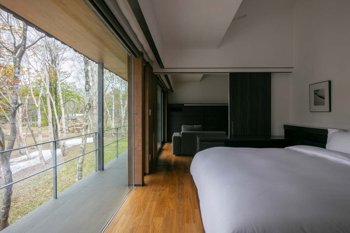 A Yoshitsu bedroom opens along full-height glass to the birch woods.